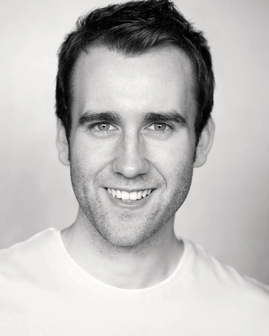 Black and white portrait of actor Matthew Lewis smiling, wearing a white T-shirt