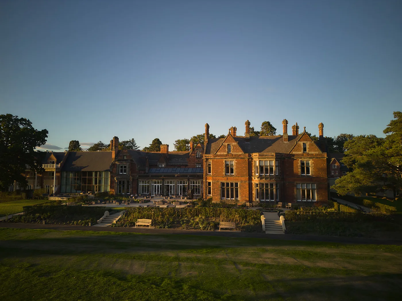 Rockliffe's red-brick main building at sunset, with new terraced planting, benches and steps leading down to the lawn in front