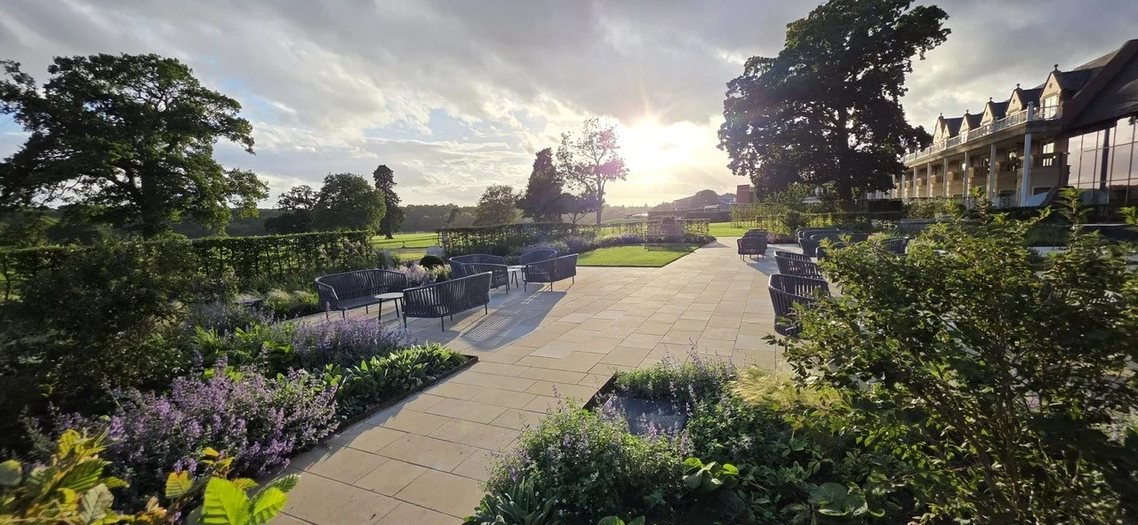 Low evening sun over a wide paved terrace at Rockliffe, with lavender-coloured flowers and shrubs in the foreground and a long two-storey building on the right